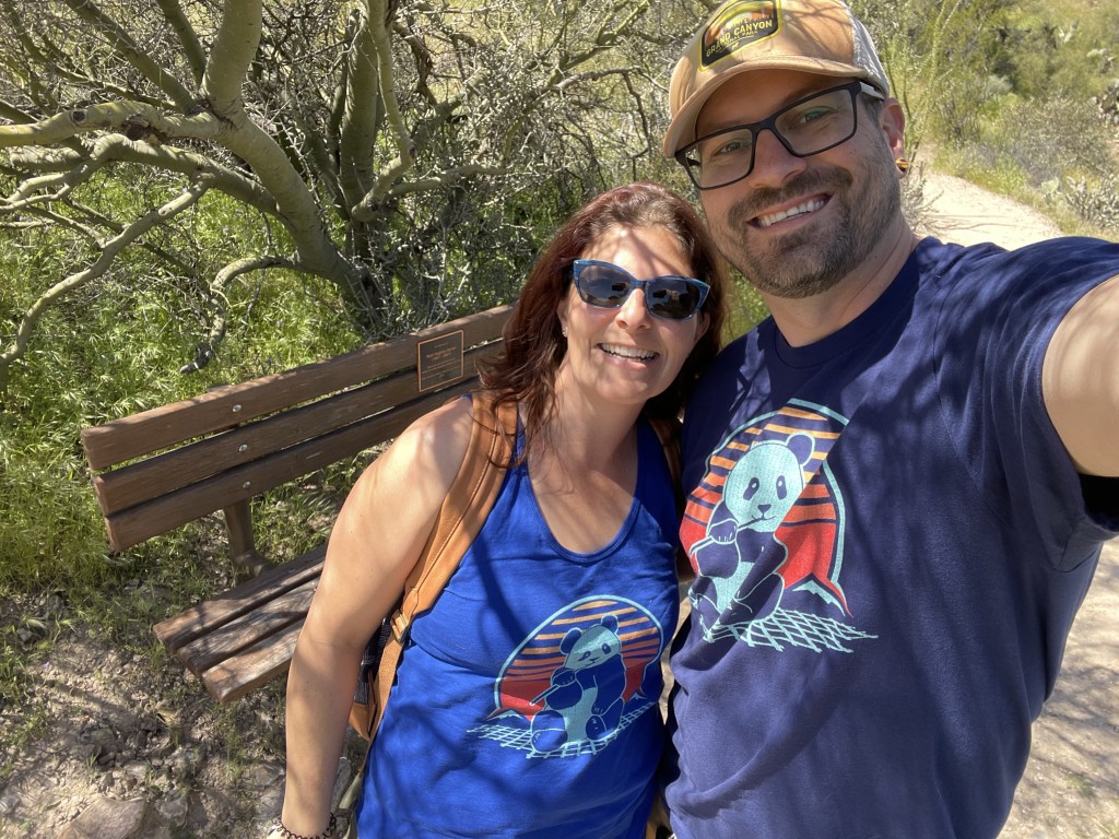 A man and a woman posing with matching shirts outside.